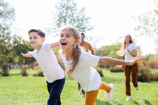 Children play outdoors in an open grassy area.